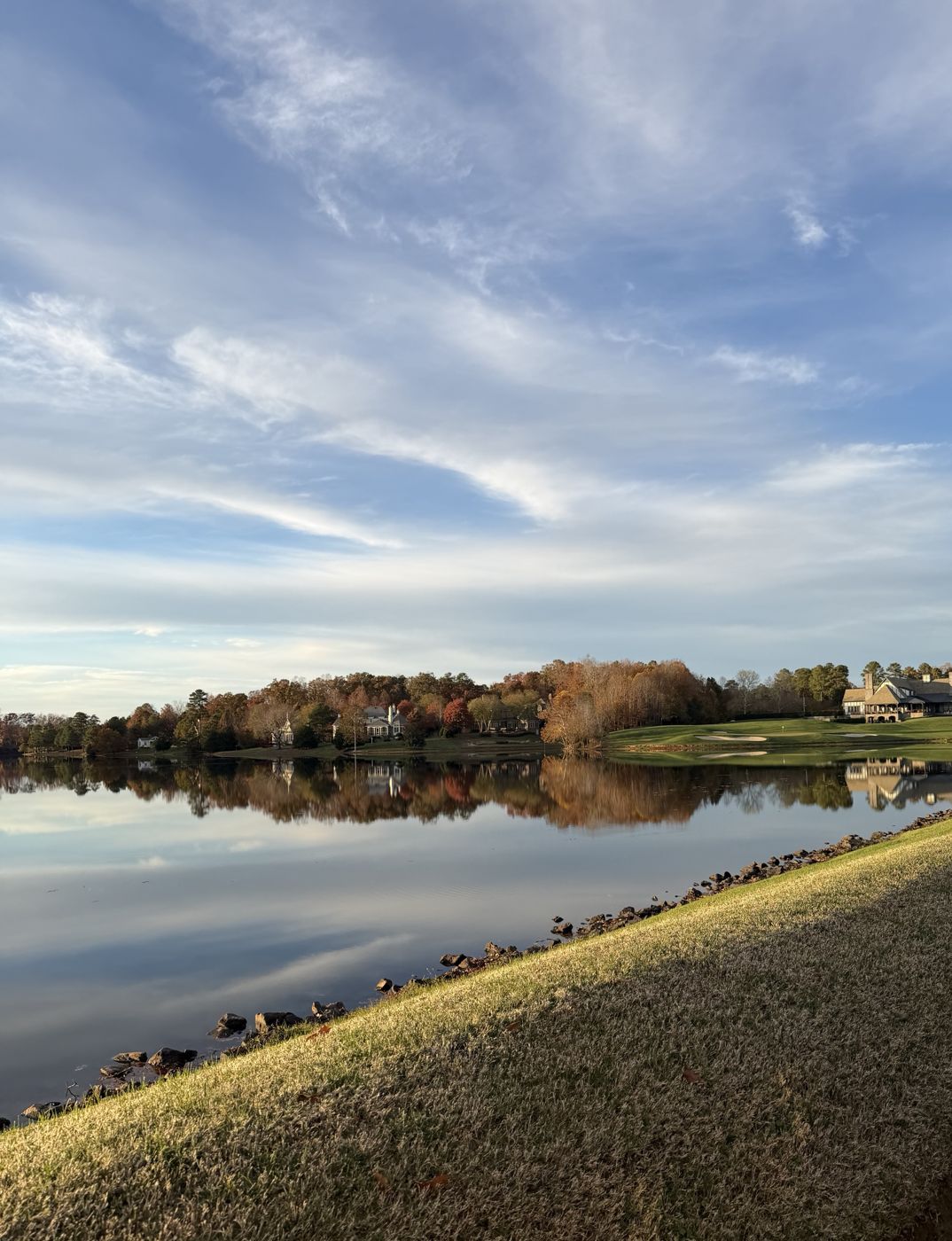 Calm lake at Kinloch reflecting fall trees, with a green and clubhouse on the far shore