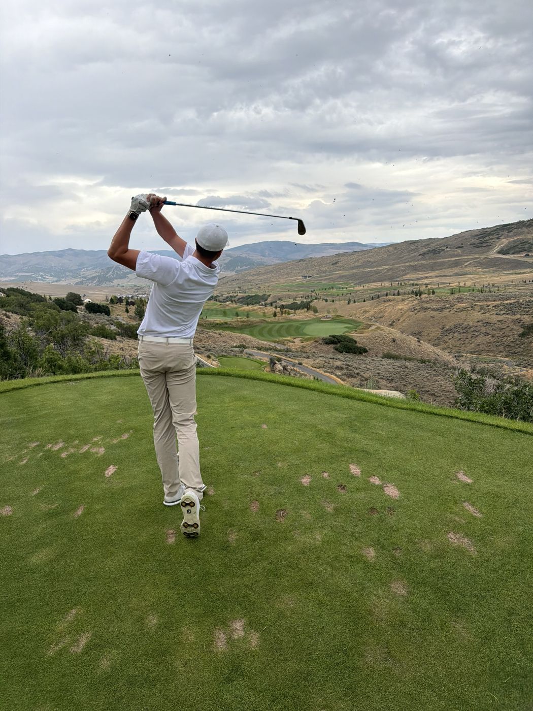 Cole finishing an iron swing on an elevated tee above a mountain valley
