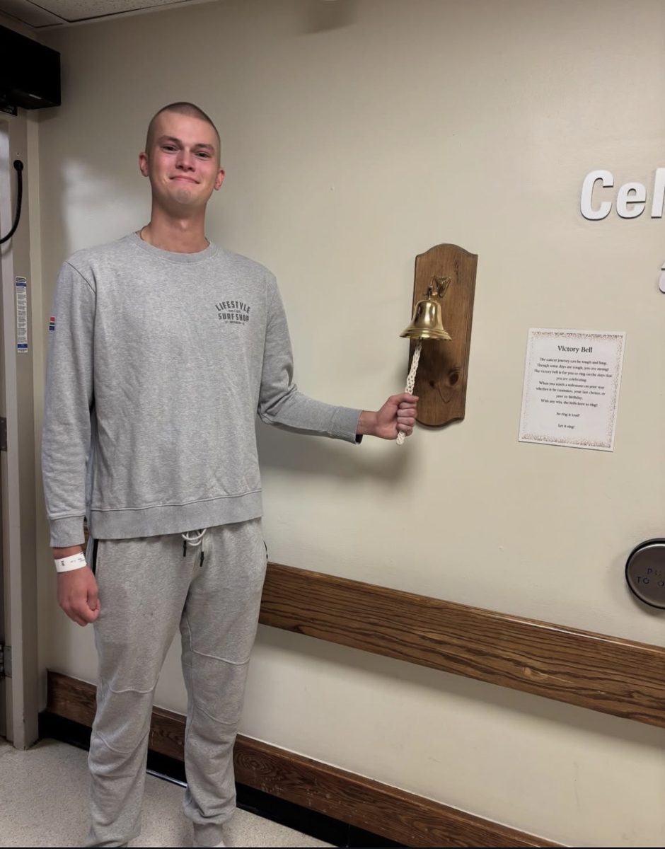 Cole smiling as he rings the brass victory bell on a hospital wall at the end of treatment